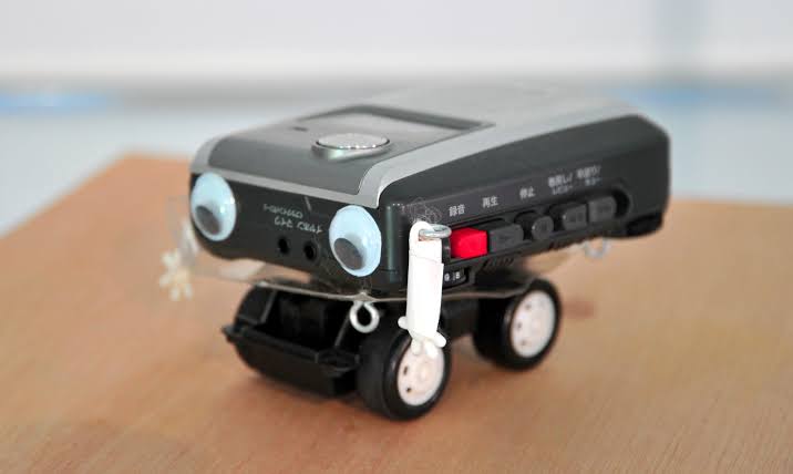 A cassette recorder with googly eyes, mounted on toy car wheels