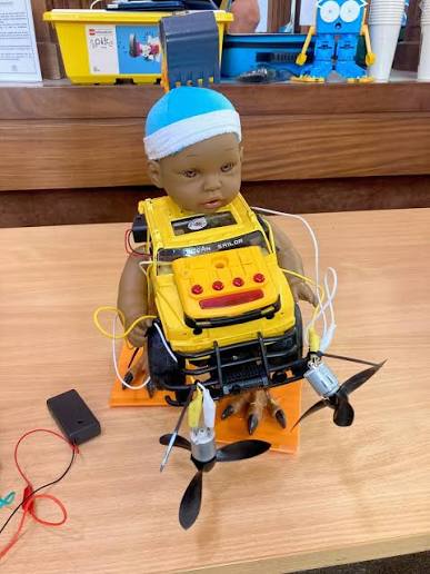 A baby doll with a toy radio strapped to its chest and a propeller for a leg